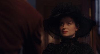 Movie still from “Tesla” (2020), directed by Michael Almereyda – A woman in a black dress and a black hat; Close Up shot, Over the shoulder angle