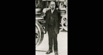 Movie still from “Tesla” (2020), directed by Michael Almereyda – An older man standing in front of a machine; Medium shot, Low angle