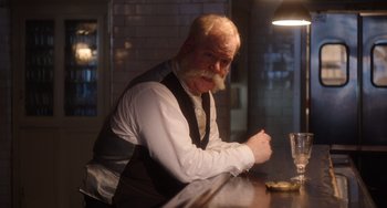 Movie still from “Tesla” (2020), directed by Michael Almereyda – An older man sitting at a table in a restaurant; Medium shot, Low angle