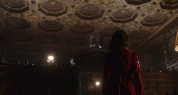 Movie still from “Tesla” (2020), directed by Michael Almereyda – A woman in a red coat standing in front of a fireplace; Extreme Wide shot, Low angle