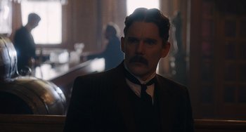 Movie still from “Tesla” (2020), directed by Michael Almereyda – A man in a suit and tie in a dark room; Close Up shot, Over the shoulder angle