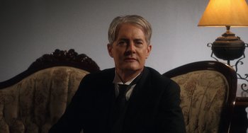 Movie still from “Tesla” (2020), directed by Michael Almereyda – A man in a suit and tie sitting in a chair; Close Up shot, Low angle
