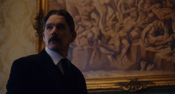 Movie still from “Tesla” (2020), directed by Michael Almereyda – A man in a suit standing in front of a painting; Medium shot, Low angle
