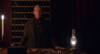 Movie still from “Tesla” (2020), directed by Michael Almereyda – An older man sitting at a table in front of an oil lamp; Medium shot, Low angle
