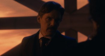 Movie still from “Tesla” (2020), directed by Michael Almereyda – A man in a suit and tie in a dark room; Close Up shot, Over the shoulder angle