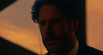 Movie still from “Tesla” (2020), directed by Michael Almereyda – A person wearing a suit and glasses; Close Up shot, Over the shoulder angle