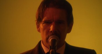 Movie still from “Tesla” (2020), directed by Michael Almereyda – A man in a suit is singing into a microphone; Close Up shot, Over the shoulder angle