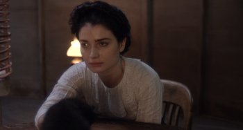Movie still from “Tesla” (2020), directed by Michael Almereyda – A woman sitting at a wooden table in front of a lamp; Close Up shot, Over the shoulder angle