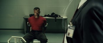 Movie still from “Blade: Trinity” (2004), directed by David S. Goyer – A man in a red shirt sitting in a room; Medium shot, Over the shoulder angle