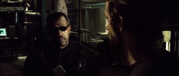 Movie still from “Blade: Trinity” (2004), directed by David S. Goyer – A man wearing sunglasses and a black jacket is talking to another man in a dark room; Close Up shot, Over the shoulder angle