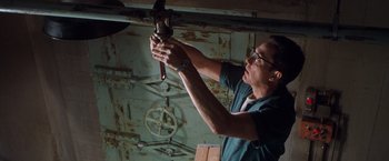 Movie still from “Blast from the Past” (1999), directed by Hugh Wilson – A man holding a pipe wrench in his hands; Medium shot, Low angle