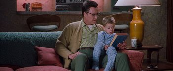 Movie still from “Blast from the Past” (1999), directed by Hugh Wilson – A man and a boy sitting on a couch reading a book; Medium shot, Low angle