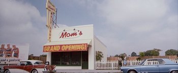 Movie still from “Blast from the Past” (1999), directed by Hugh Wilson – A store front with a sign that says " mom's grand opening "; Wide shot, Low angle