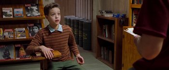Movie still from “Blast from the Past” (1999), directed by Hugh Wilson – A young boy sitting in a room holding a book; Medium shot, High angle