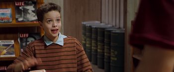 Movie still from “Blast from the Past” (1999), directed by Hugh Wilson – A young boy standing in front of a bunch of books; Close Up shot, High angle
