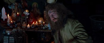 Movie still from “Blast from the Past” (1999), directed by Hugh Wilson – A man with long hair and a long beard is sitting in front of candles; Medium shot, Over the shoulder angle