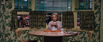 Movie still from “Blast from the Past” (1999), directed by Hugh Wilson – A woman sitting at a table with a cup of coffee; Medium shot, High angle