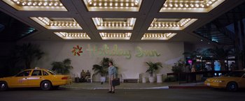 Movie still from “Blast from the Past” (1999), directed by Hugh Wilson – A man standing in front of a hotel lobby; Extreme Wide shot, Low angle