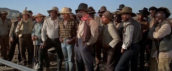 Movie still from “Blazing Saddles” (1974), directed by Mel Brooks – A group of men standing next to each other on top of a hill; Medium shot, High angle