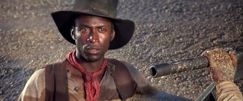 Movie still from “Blazing Saddles” (1974), directed by Mel Brooks – A man in a cowboy hat with a gun in his hand; Close Up shot, Low angle