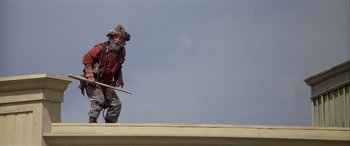 Movie still from “Blazing Saddles” (1974), directed by Mel Brooks – An old man with a beard and a hat is walking on a roof; Medium shot, Low angle
