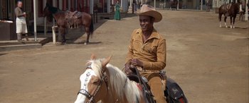Movie still from “Blazing Saddles” (1974), directed by Mel Brooks – A man sitting on top of a horse in the dirt; Medium shot, Over the shoulder angle