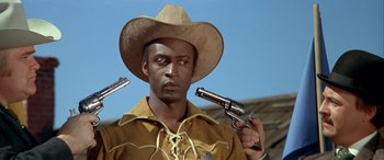 Movie still from “Blazing Saddles” (1974), directed by Mel Brooks – A man in a cowboy hat holding two guns; Medium shot, Low angle