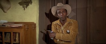 Movie still from “Blazing Saddles” (1974), directed by Mel Brooks – A man wearing a cowboy hat and holding a pair of pistols; Medium shot, Over the shoulder angle