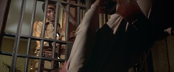 Movie still from “Blazing Saddles” (1974), directed by Mel Brooks – A man in a jail cell with another man in a jail cell behind bars; Medium shot, Over the shoulder angle