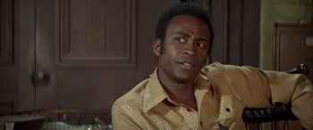 Movie still from “Blazing Saddles” (1974), directed by Mel Brooks – A person sitting in a room; Close Up shot, Over the shoulder angle