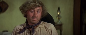 Movie still from “Blazing Saddles” (1974), directed by Mel Brooks – A person sitting in a chair wearing a neck tie; Close Up shot, Over the shoulder angle