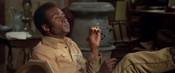 Movie still from “Blazing Saddles” (1974), directed by Mel Brooks – A man smoking a cigarette while holding a cigarette; Medium shot, Low angle