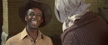 Movie still from “Blazing Saddles” (1974), directed by Mel Brooks – A man in a cowboy hat smiles at a woman in a dress; Close Up shot, Over the shoulder angle