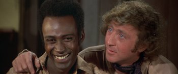 Movie still from “Blazing Saddles” (1974), directed by Mel Brooks – Two men smiling for the camera in a room; Close Up shot, Over the shoulder angle
