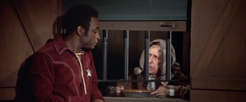 Movie still from “Blazing Saddles” (1974), directed by Mel Brooks – A man and a woman sitting in front of a jail cell; Medium shot, Over the shoulder angle