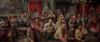 Movie still from “Blazing Saddles” (1974), directed by Mel Brooks – A group of men in cowboy hats are sitting in front of a window; Wide shot, High angle
