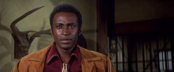 Movie still from “Blazing Saddles” (1974), directed by Mel Brooks – A man in a red shirt and a brown jacket; Close Up shot, Low angle