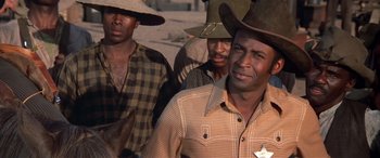 Movie still from “Blazing Saddles” (1974), directed by Mel Brooks – A group of men standing next to each other; Close Up shot, Over the shoulder angle