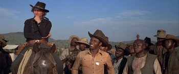 Movie still from “Blazing Saddles” (1974), directed by Mel Brooks – A group of men standing next to each other in a field; Medium shot, Low angle