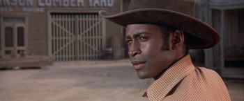 Movie still from “Blazing Saddles” (1974), directed by Mel Brooks – A man wearing a cowboy hat in front of a building; Close Up shot, Low angle
