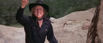 Movie still from “Blazing Saddles” (1974), directed by Mel Brooks – A man wearing a cowboy hat standing in the dirt; Medium shot, Low angle