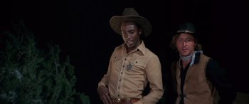 Movie still from “Blazing Saddles” (1974), directed by Mel Brooks – A man wearing a cowboy hat holding a gun; Medium shot, Low angle