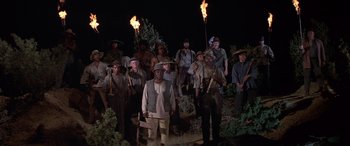 Movie still from “Blazing Saddles” (1974), directed by Mel Brooks – A group of men standing next to each other holding torches; Wide shot, High angle