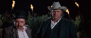Movie still from “Blazing Saddles” (1974), directed by Mel Brooks – A man wearing a cowboy hat standing in front of a cross; Medium shot, Low angle