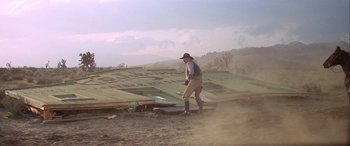 Movie still from “Blazing Saddles” (1974), directed by Mel Brooks – A man standing in a dirt field next to a pile of wood; Wide shot, Low angle