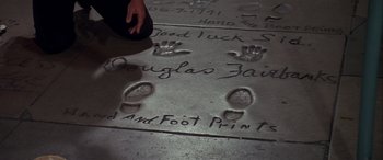 Movie still from “Blazing Saddles” (1974), directed by Mel Brooks – A person is looking at a hand and foot print on the sidewalk; Extreme Close Up shot, High angle