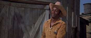 Movie still from “Blazing Saddles” (1974), directed by Mel Brooks – A man wearing a cowboy hat standing in front of a barn; Medium shot, Low angle