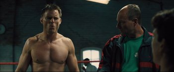 Movie still from “Bleed for This” (2016), directed by Ben Younger – A man standing next to another man in a boxing ring; Medium shot, Over the shoulder angle