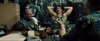 Movie still from “Bleed for This” (2016), directed by Ben Younger – A man sitting at a table with his arms up; Medium shot, Over the shoulder angle