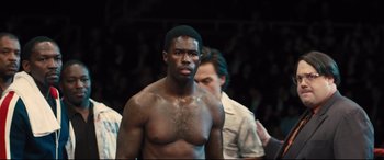 Movie still from “Bleed for This” (2016), directed by Ben Younger – A man with no shirt standing in front of a group of people; Close Up shot, High angle
